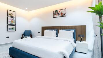 A modern bedroom with a large bed, a bedside table, a chair, and artwork on the wall.