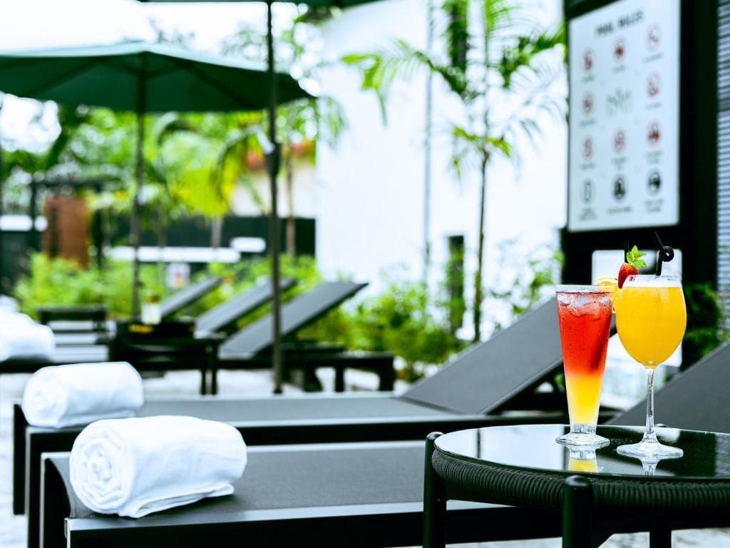 Un área junto a la piscina con sillones de descanso y una mesa con bebidas.