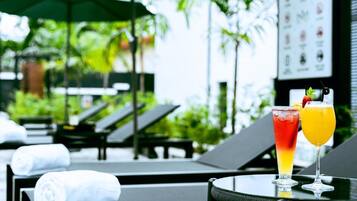 Un área junto a la piscina con sillones de descanso y una mesa con bebidas.