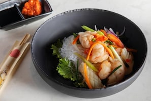 A bowl of shrimp and vegetables with a side of dipping sauce.