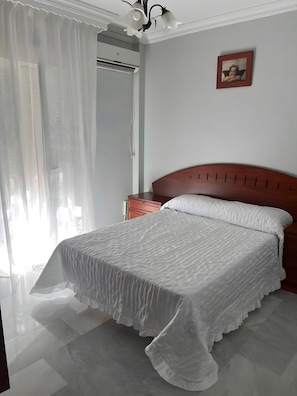 Un dormitorio con una cama, una mesita de noche, un equipo de aire acondicionado instalado en la pared y un cuadro enmarcado.
