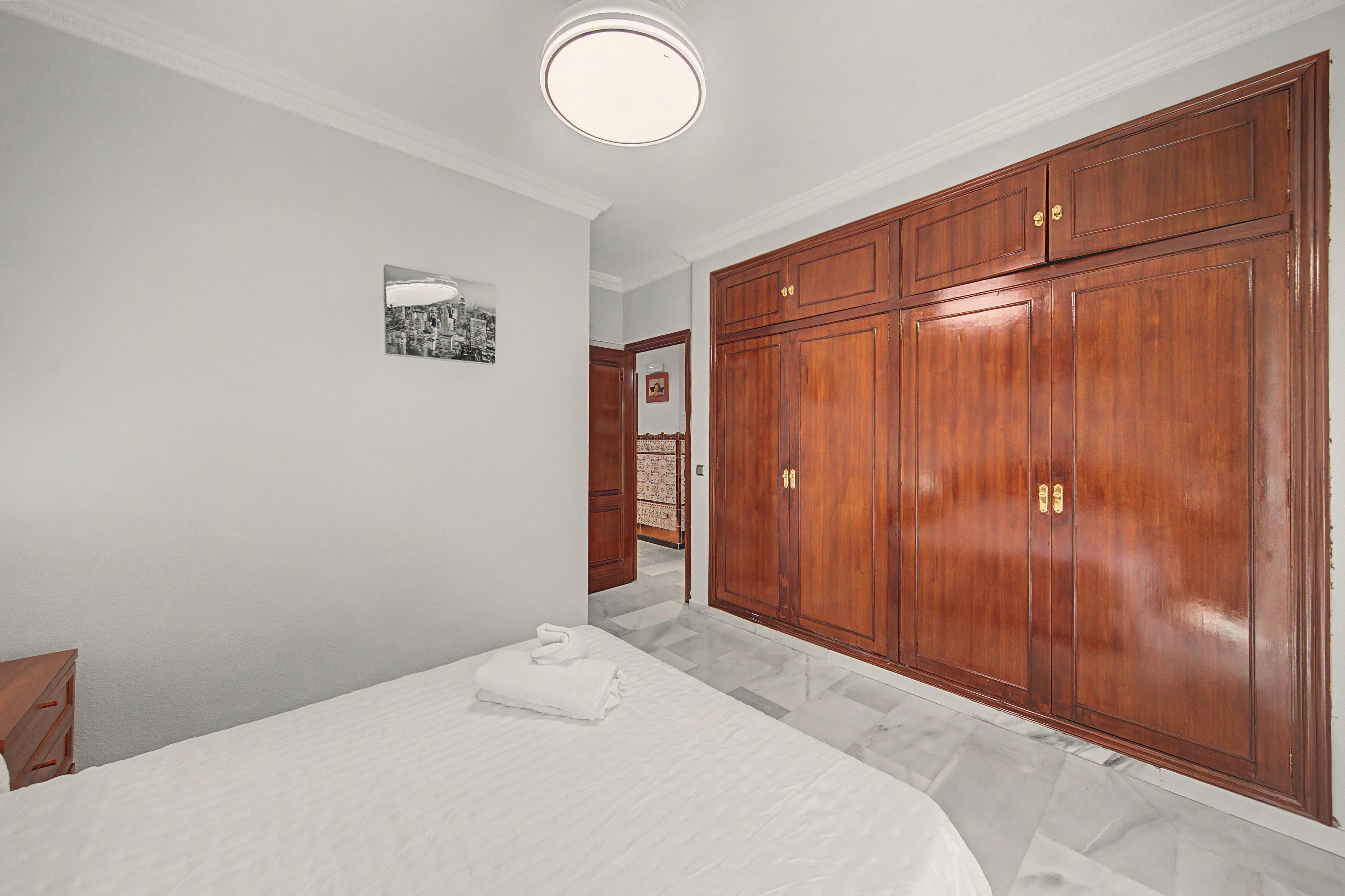 Een slaapkamer met een groot bed, een houten garderobe en een klein fotolijstje aan de muur.