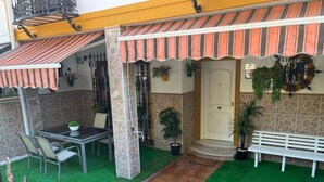 Un patio al aire libre con una mesa, sillas, un banco y plantas en macetas.
