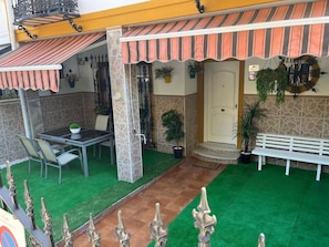 Un patio al aire libre con una mesa, sillas, un banco y plantas en macetas.