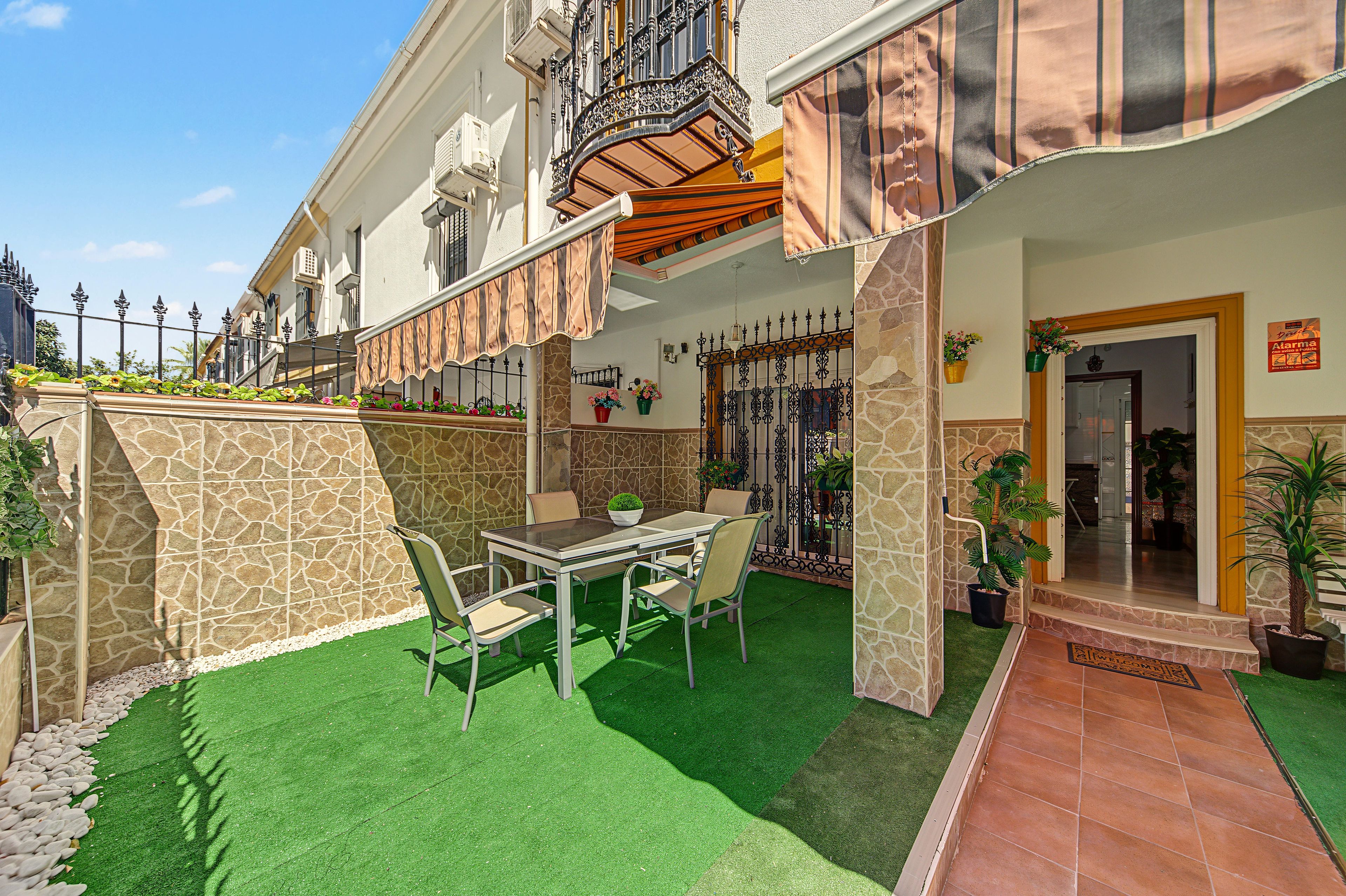 Un patio de hotel con una mesa y sillas de vidrio, un muro de piedra y una zona con césped artificial verde.