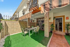 A hotel courtyard with a glass table and chairs, a stone wall, and a green artificial turf area. - Casa Alicia — Spacious Apartment with Free Parking in Seville (Sevilla)