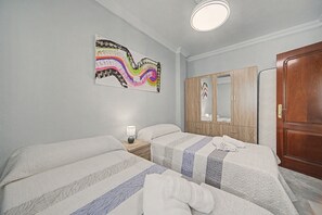 A bedroom with two beds, a wooden wardrobe, a mirror, and a wall-mounted artwork. - Casa Alicia — Spacious Apartment with Free Parking in Seville (Sevilla)