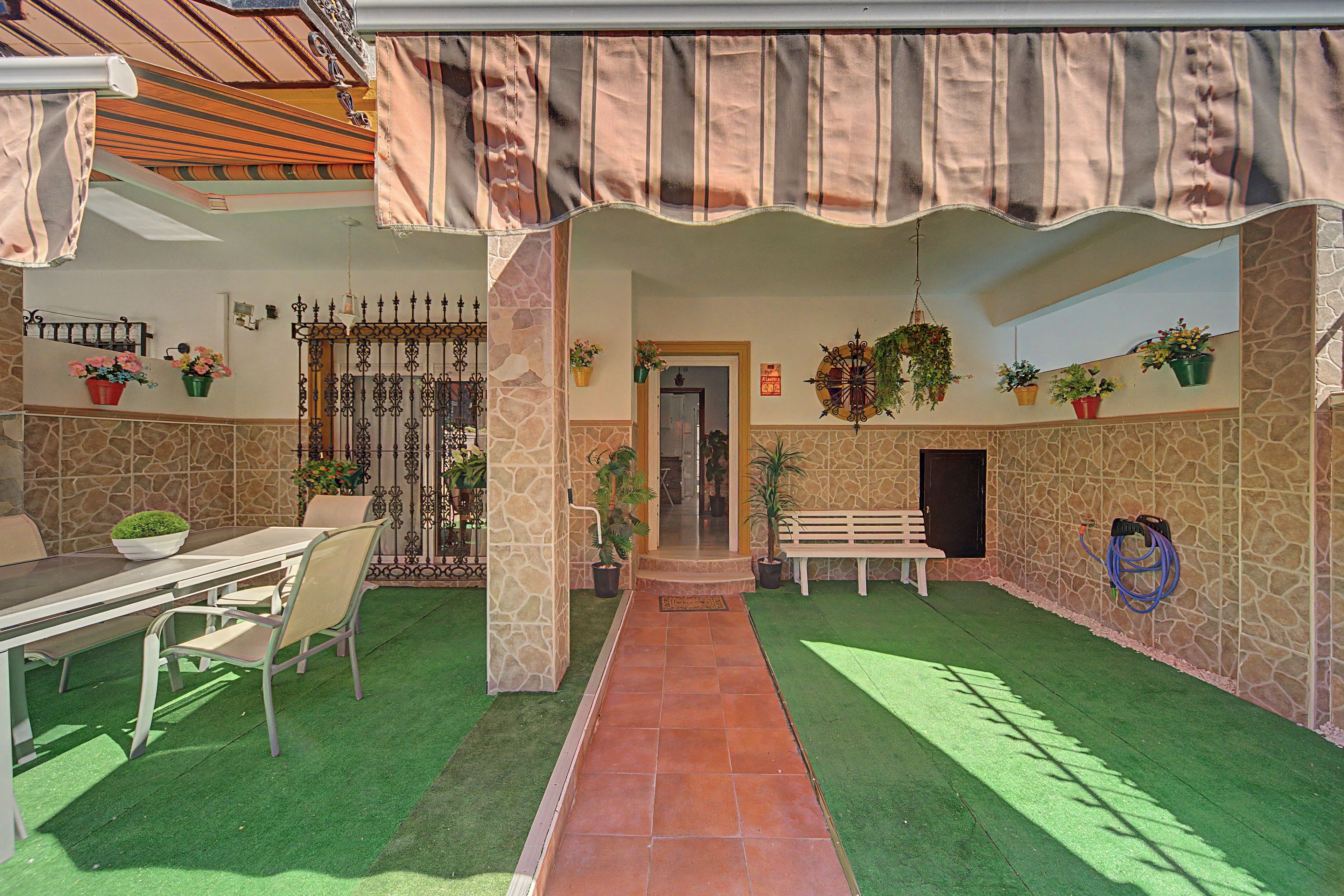 A covered outdoor area with a dining table, chairs, a bench, and potted plants.