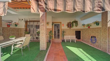 A covered outdoor area with a dining table, chairs, a bench, and potted plants.