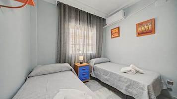 Hotellihuone, jossa on kaksi erillistä sänkyä, yöpöytä, lamppu ja kaksi seinälle ripustettua taulua.