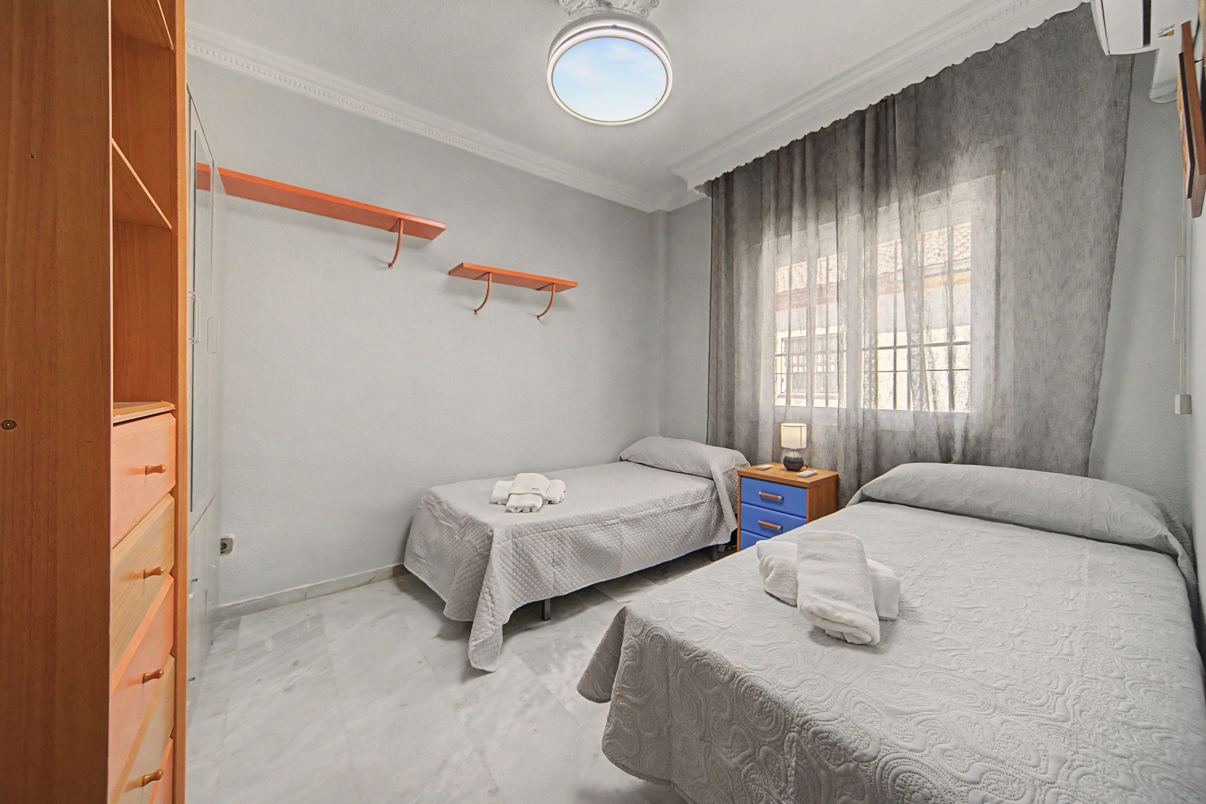 A bedroom with two beds, a wardrobe, a nightstand, and a window with curtains.
