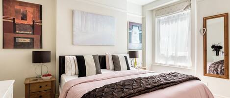 Un dormitorio con cama, mesitas de noche, una ventana con cortinas y decoración en la pared.