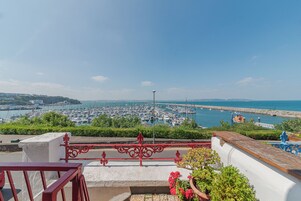 A coastal view with a marina, a clear sky, and a balcony with a railing.