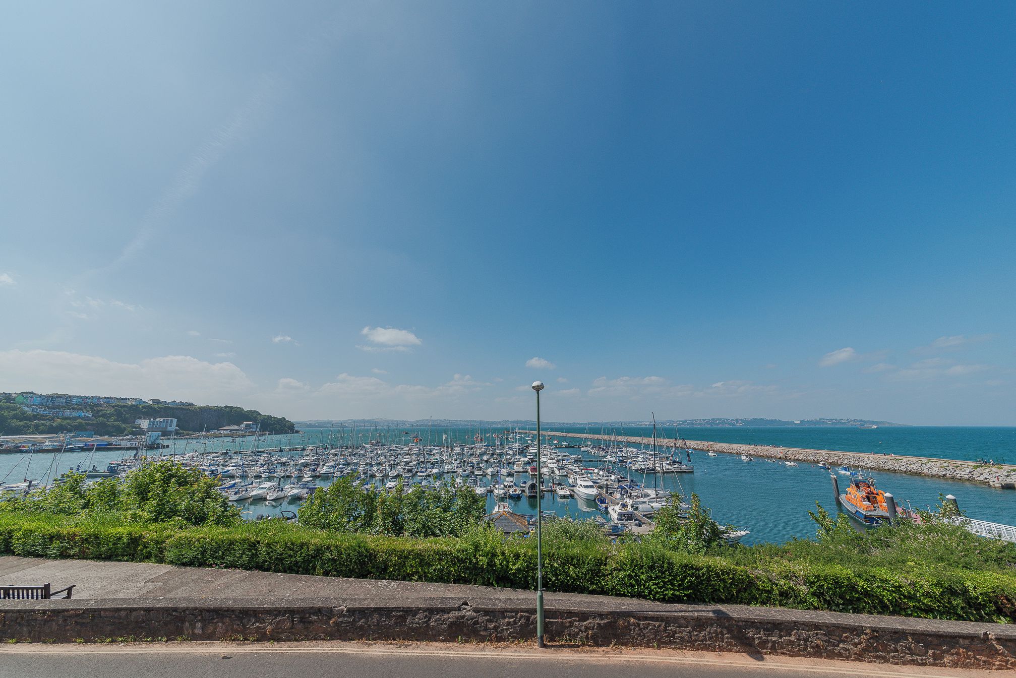 Marina com vários barcos atracados, céu claro e costa rochosa.