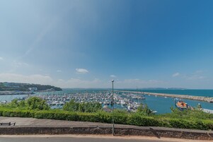 Un puerto deportivo con numerosos barcos amarrados, un cielo despejado y una costa rocosa.