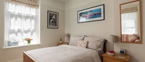 Quarto com cama, mesas de cabeceira, um espelho e uma janela com cortinas.
