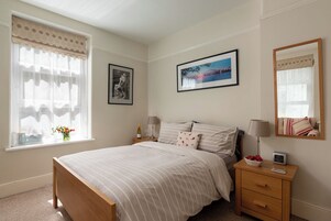 A bedroom with a bed, bedside tables, a nightstand, a mirror, and a window with curtains.