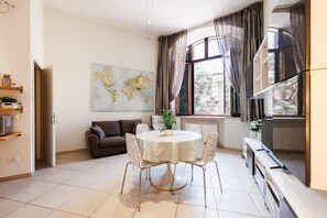 A living room with a round table, a sofa, a world map on the wall, and a large window with curtains. - Bright and cozy 70 sqm apartment, accommodating up to 5 guests, located on the ground floor of an elegant, renovated building dating back to the early 20th century (access involves a few steps). The property is located in a quiet neighborhood offering al (Siena)
