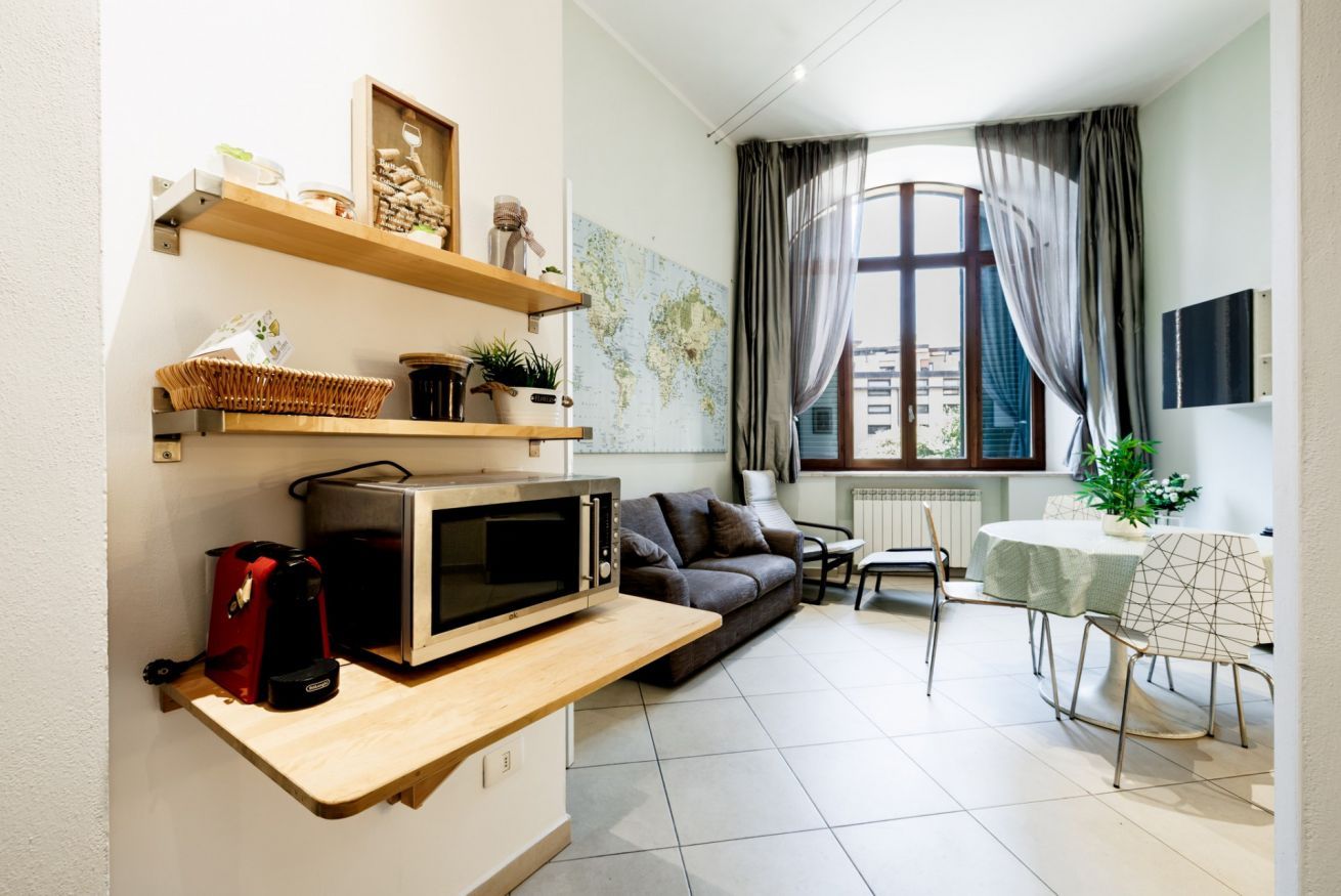 A compact living space with a kitchenette, a sofa, a dining table, and a large window with curtains.