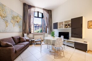Een moderne woonkamer met een bank, een eettafel, stoelen, een flatscreen televisie, een wereldkaart en een raam met gordijnen.