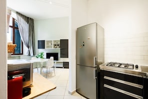 A compact kitchen with a refrigerator, stove, and a dining area with a table and chairs. - Bright and cozy 70 sqm apartment, accommodating up to 5 guests, located on the ground floor of an elegant, renovated building dating back to the early 20th century (access involves a few steps). The property is located in a quiet neighborhood offering al (Siena)