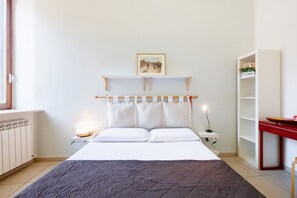 Une chambre à coucher avec un lit, des lampes de chevet, une table de chevet, une étagère avec un tableau et un radiateur.