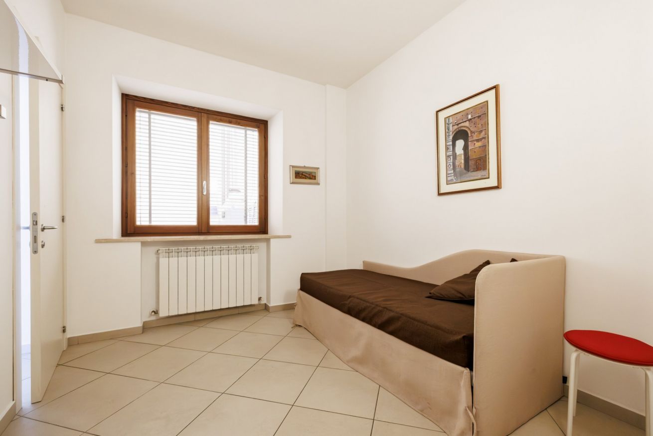 A room with a bed, a radiator, a window with blinds, a door, and a framed picture on the wall.