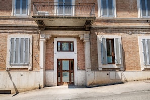 A building facade with a central entrance, multiple windows with shutters, and a balcony. - Bright and cozy 70 sqm apartment, accommodating up to 5 guests, located on the ground floor of an elegant, renovated building dating back to the early 20th century (access involves a few steps). The property is located in a quiet neighborhood offering al (Siena)