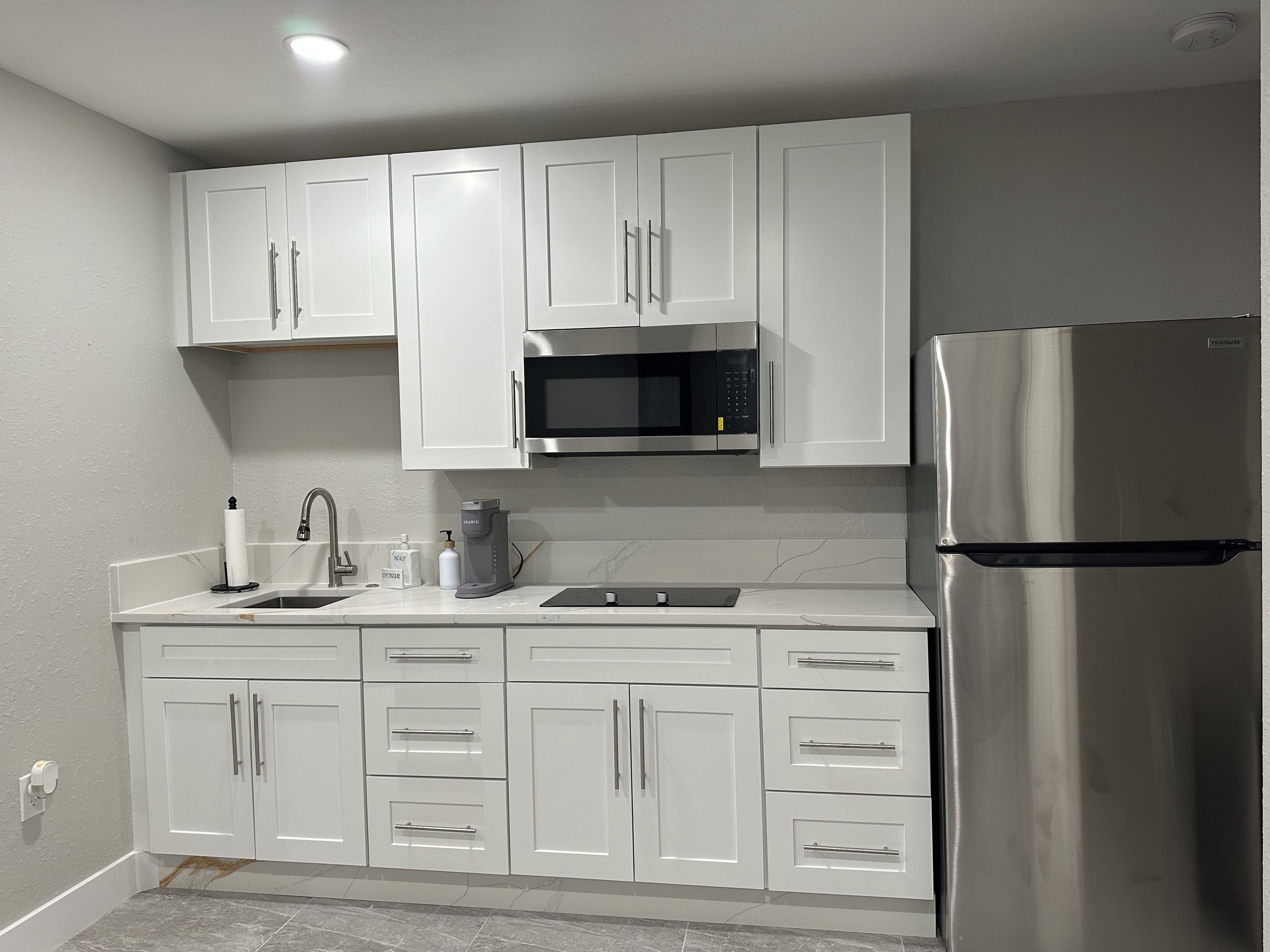 Una cocina moderna con gabinetes blancos, un refrigerador de acero inoxidable, un microondas y una cafetera.