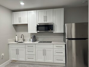 A modern kitchen with white cabinets, a stainless steel refrigerator, a microwave, and a coffee maker. - Cozy Artist Studio! (Port St. Lucie)