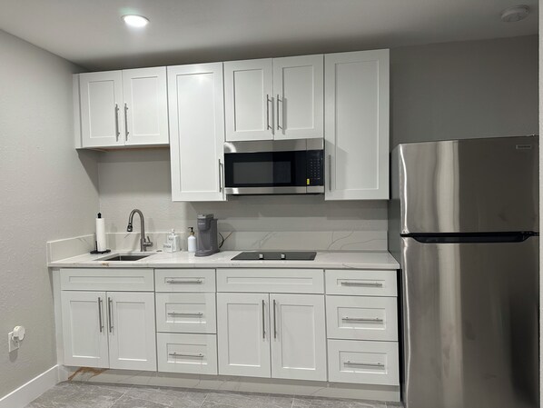 A modern kitchen with white cabinets, a stainless steel refrigerator, a microwave, and a coffee maker.