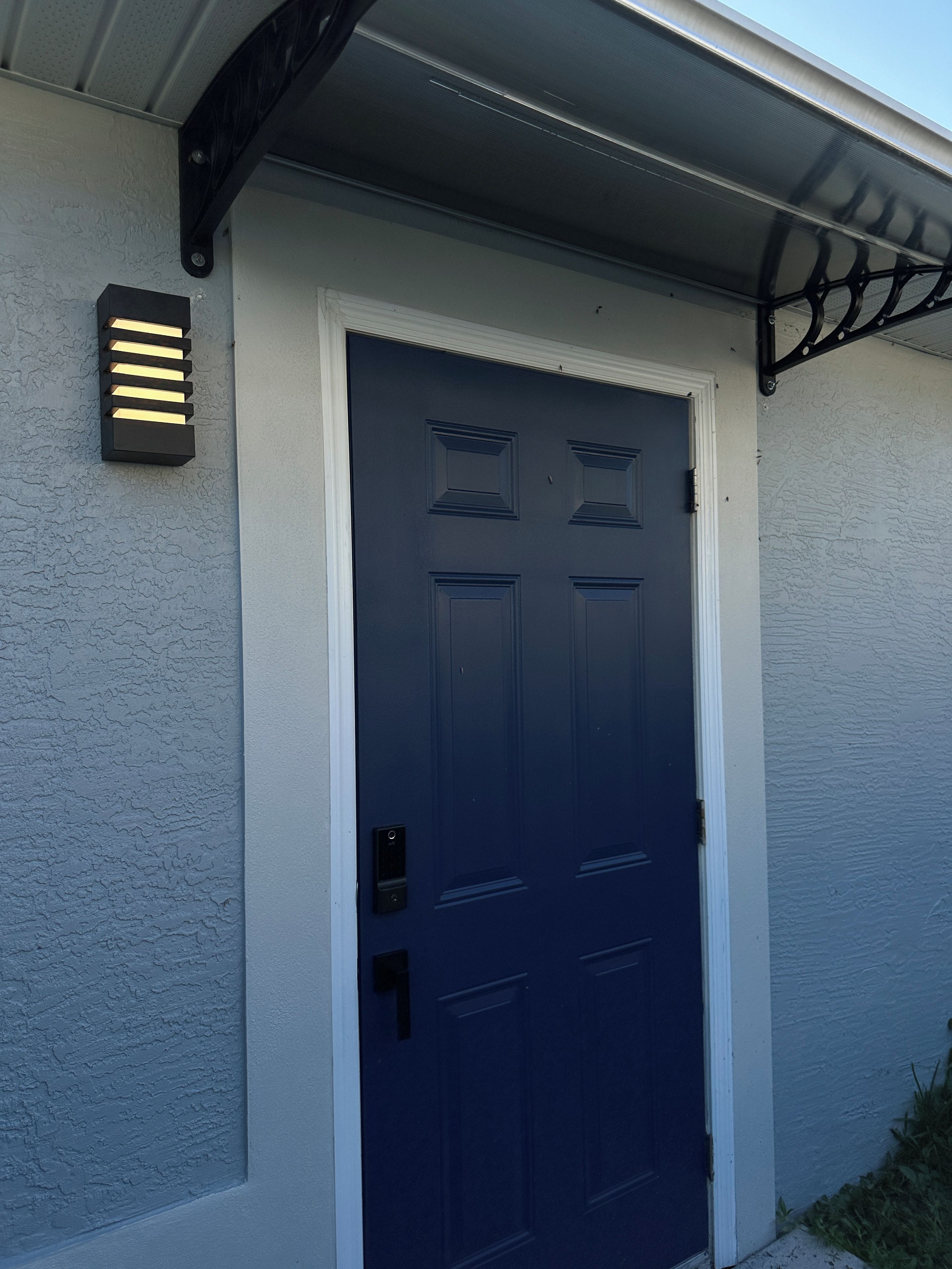 A dark blue door with a textured white wall, a small outdoor light fixture, and a metal bracket above the door.