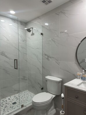 A modern bathroom with a glass-enclosed shower, a toilet, and a vanity with a mirror.