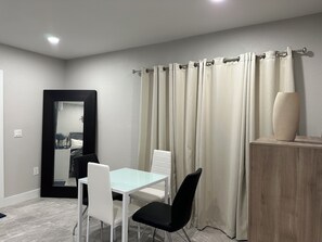 A room with a dining table, two chairs, a mirror, and a curtain.