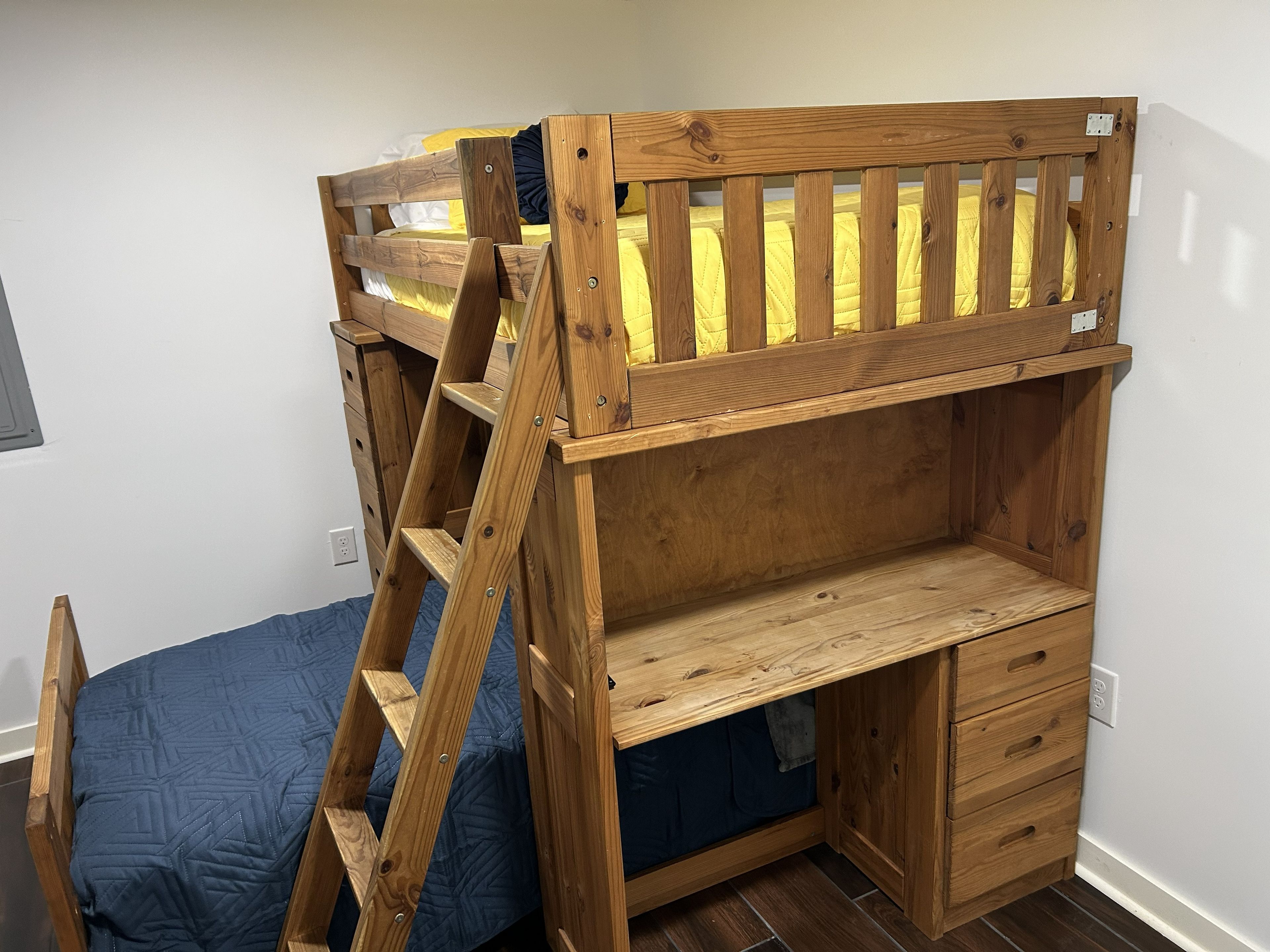 Un lit superposé avec une échelle en bois, un bureau et un meuble à tiroirs.