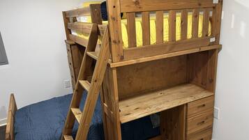 Un lit superposé avec une échelle en bois, un bureau et un meuble à tiroirs.