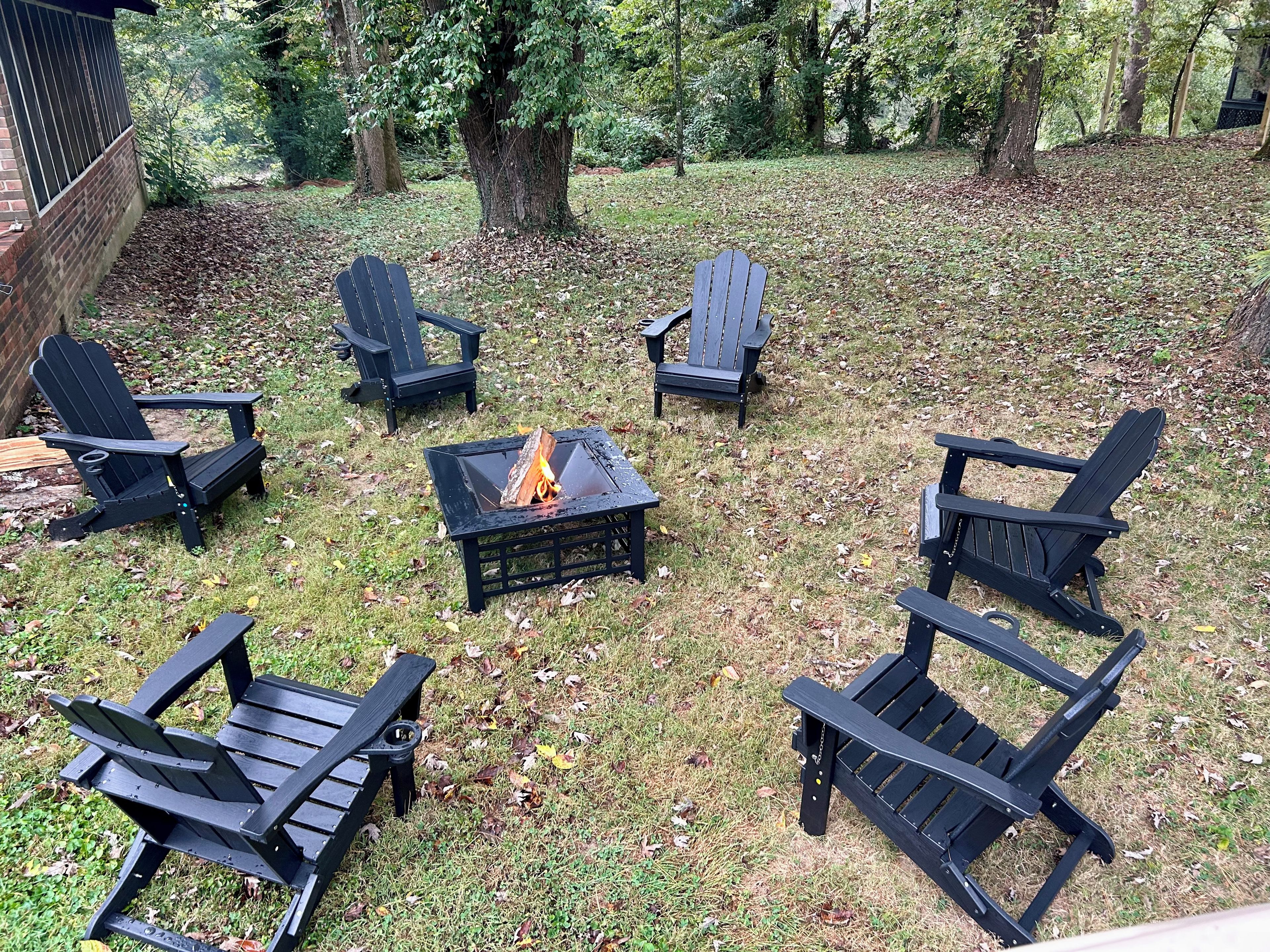 Un patio trasero con un brasero rodeado de sillas Adirondack.