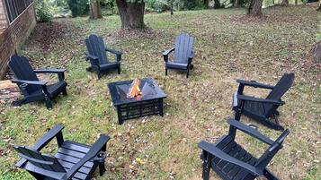 Un patio trasero con un brasero rodeado de sillas Adirondack.