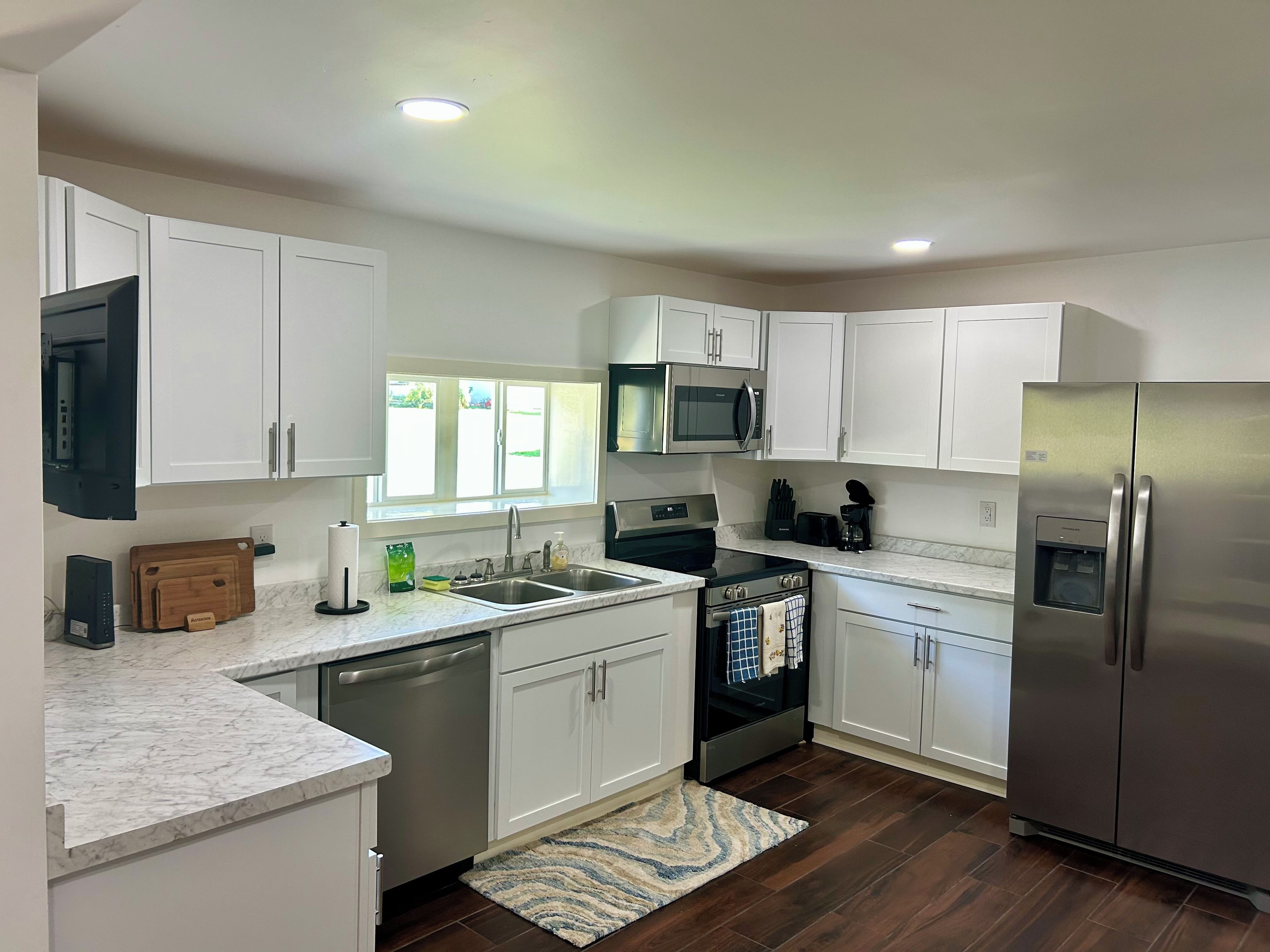 A modern kitchen with white cabinets, stainless steel appliances, and a marble countertop.