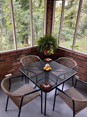 A dining area with a metal table and wicker chairs, a potted plant, and a view of trees through large windows. - Versailles Riverfront Retreat: Fully Renovated Home with Stunning River Views (Versailles)