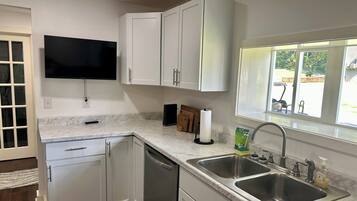 A modern kitchen with white cabinets, a built-in dishwasher, a double sink, and a flat-screen TV mounted above the countertop.