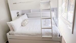 Una cama litera con escalera, ropa de cama blanca y una ventana con vistas al follaje.