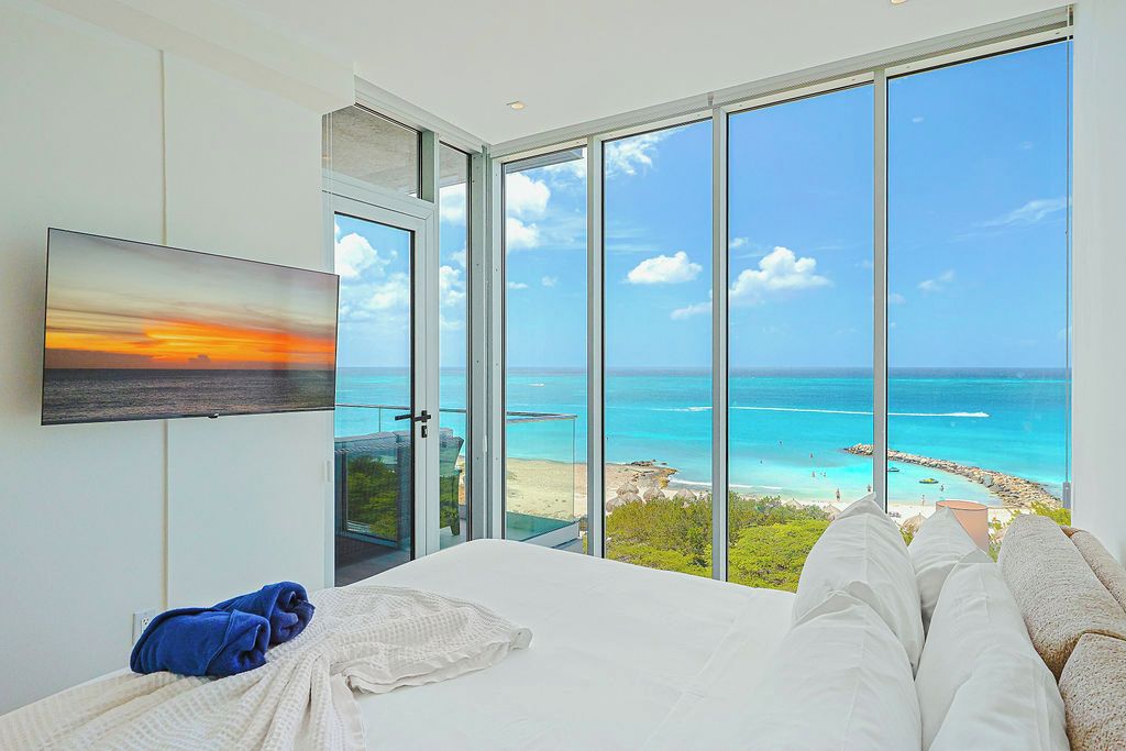 Ein Schlafzimmer mit einem großen Bett, einem Fernseher an der Wand und Meerblick durch raumhohe Fenster.