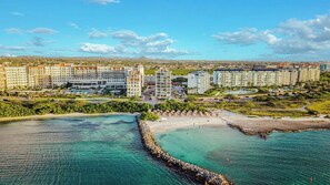 Ein Hotel an der Küste mit mehreren Gebäuden, einem Strand und klarem, türkisblauem Wasser.