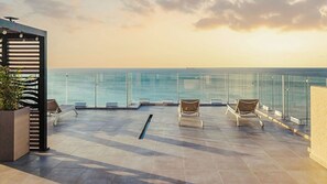 Terraço no telhado com vista para o mar, com duas espreguiçadeiras e guarda-corpo de vidro.