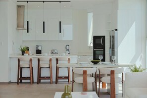 Cozinha moderna com armários brancos, uma ilha central com banquetas e eletrodomésticos embutidos.