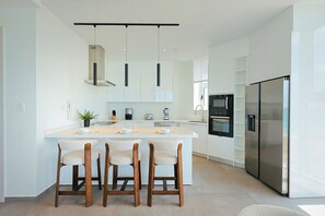 Cozinha moderna com ilha central, banquetas, forno embutido e geladeira de aço inoxidável.