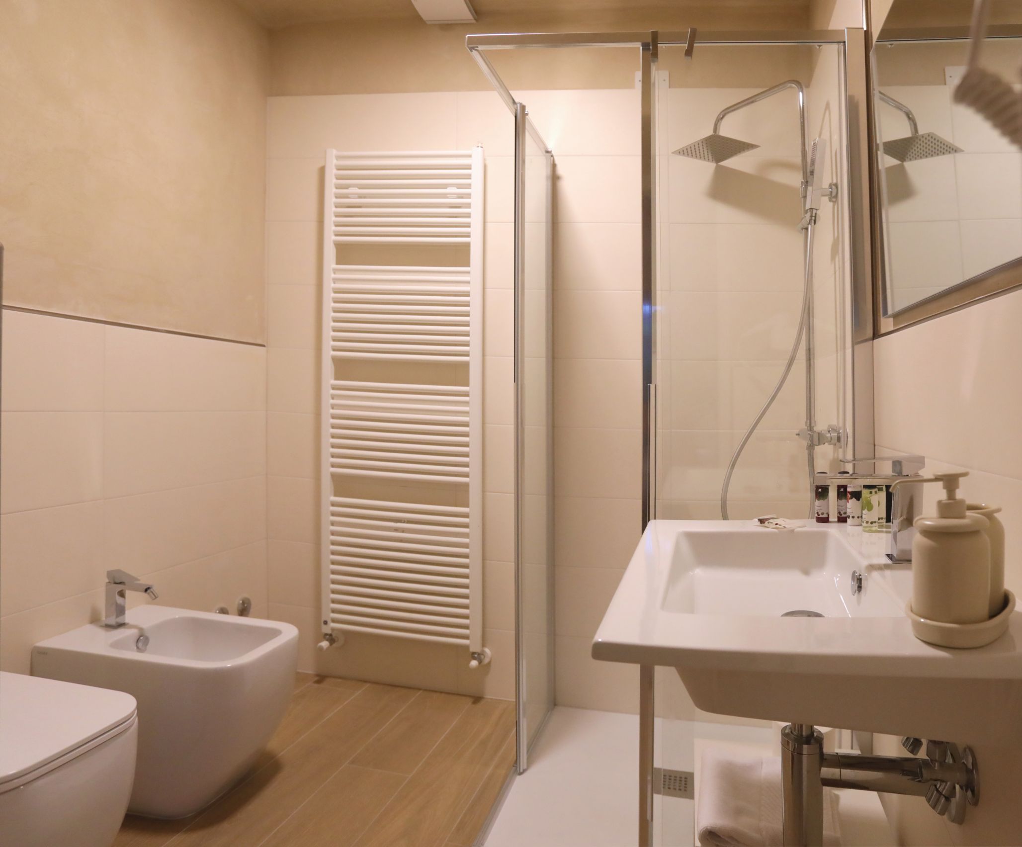 Un baño moderno con ducha de vidrio, lavamanos blanco con espejo y un bidé.