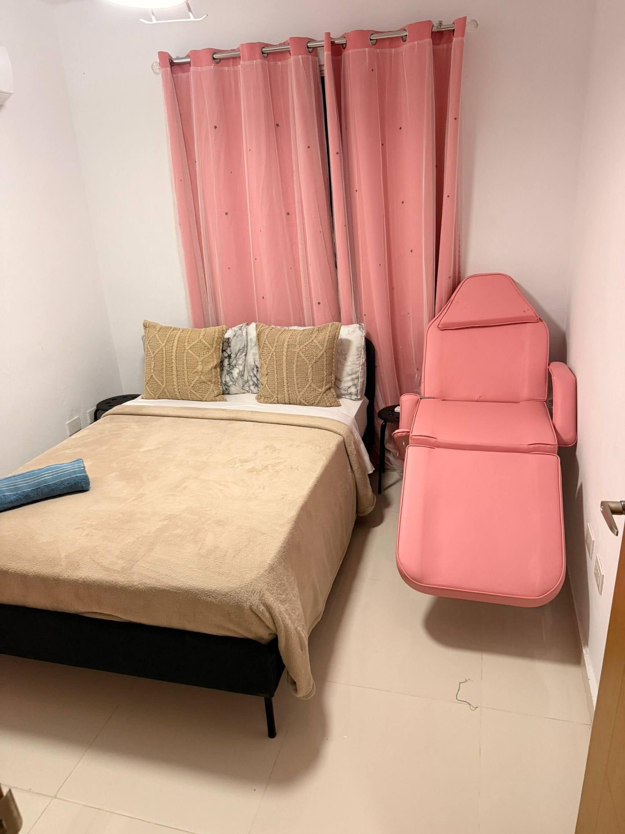 Un dormitorio con una cama, una silla rosa y cortinas rosas.