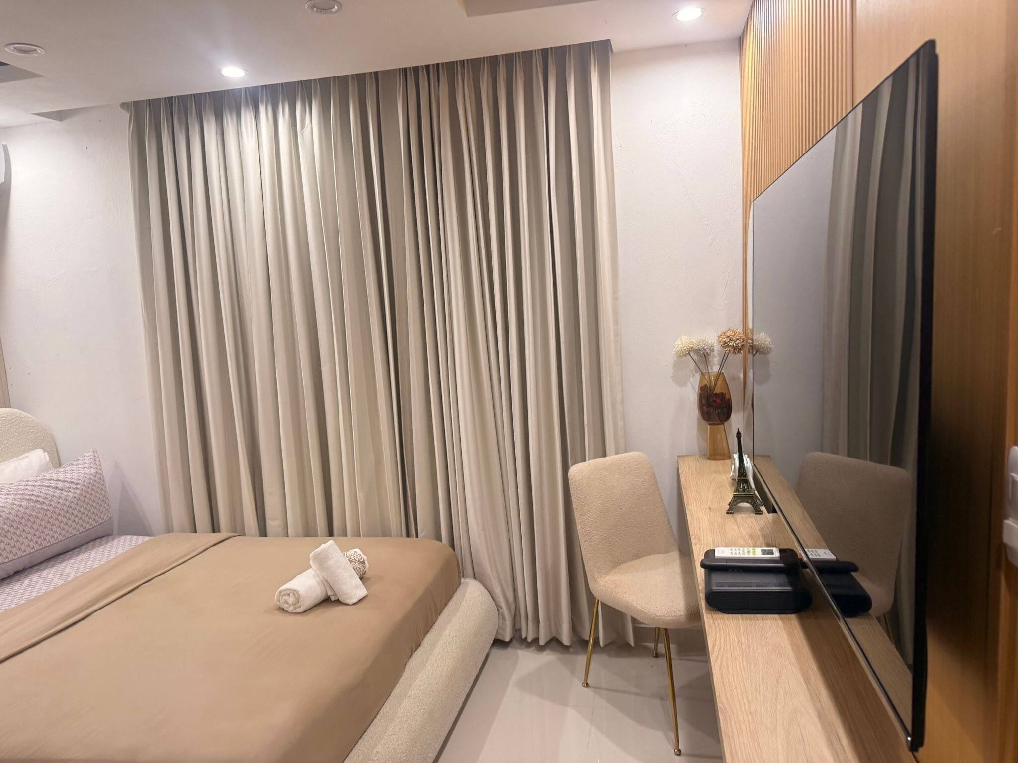 Habitación de hotel con una cama, un escritorio con televisor de pantalla plana, una silla y un jarrón con flores.